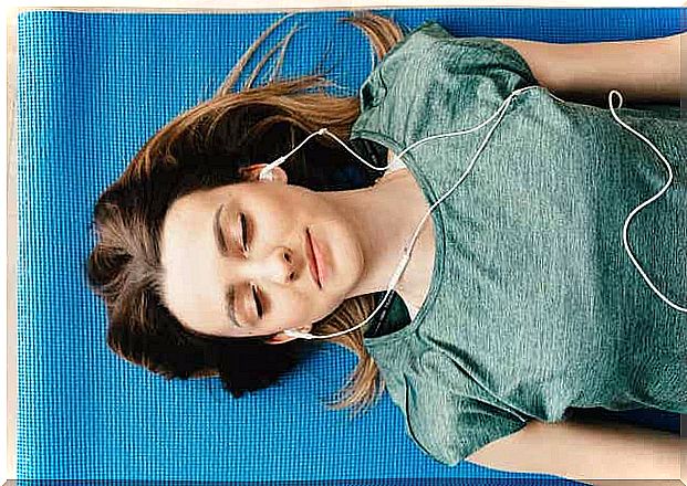 A woman lying on a mat with her eyes closed and listening to headphones.