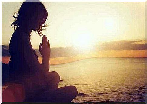 A woman meditating on the beach at sunset.